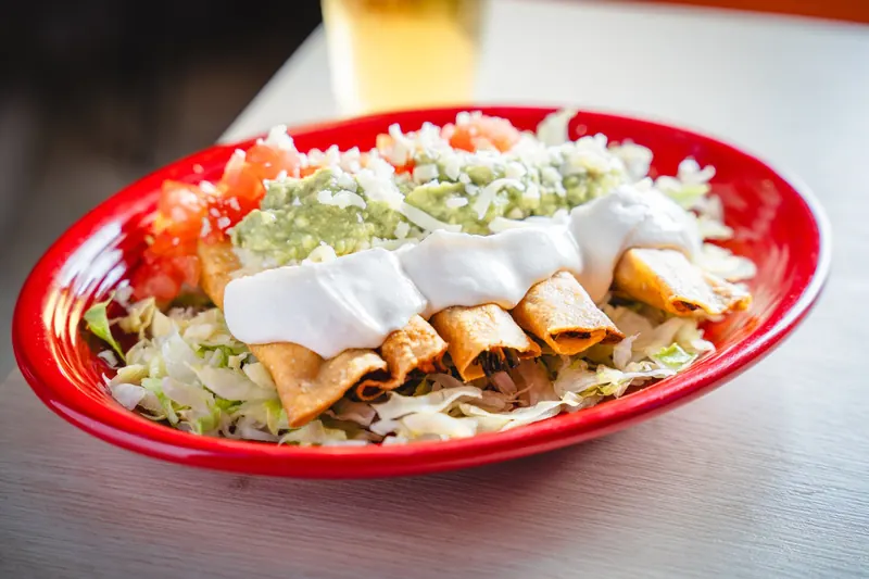 Taquitos under guacamole and sour cream on a red platter