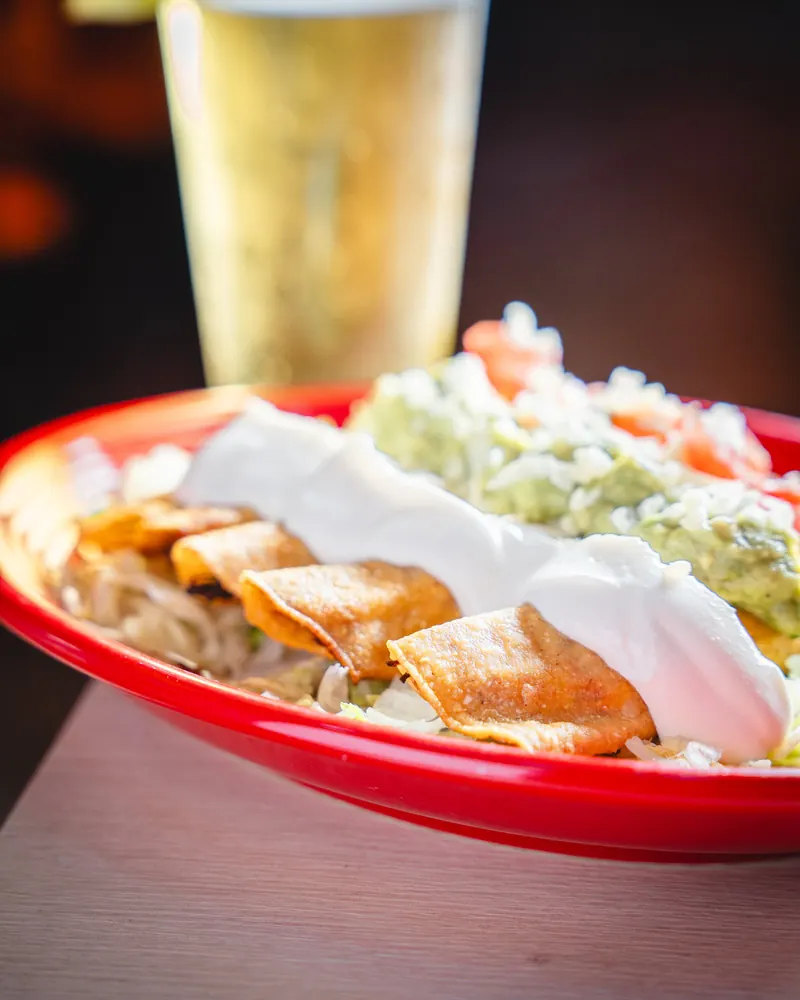 Taquitos under guacamole and sour cream on a red platter